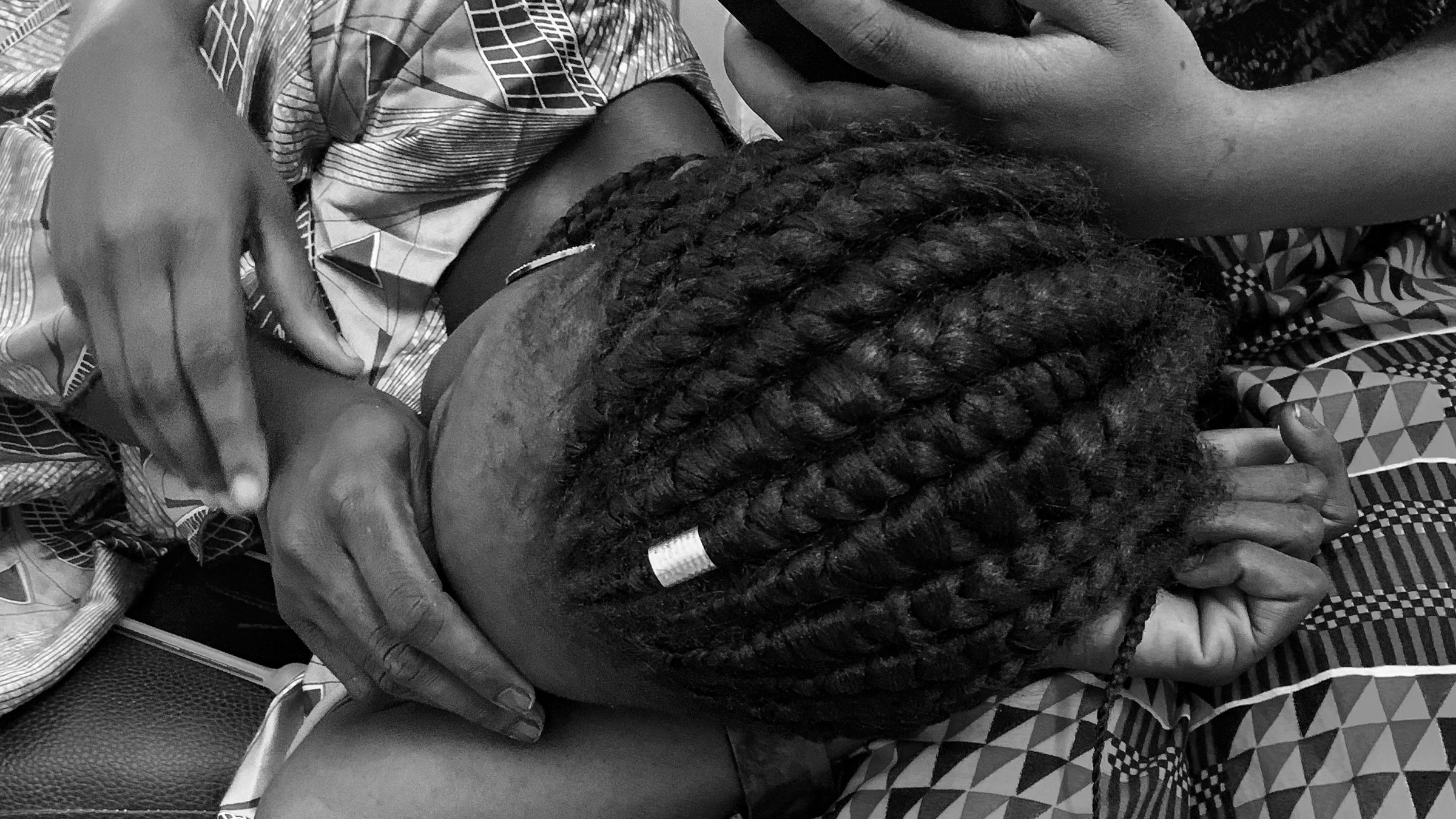 Bereft African woman - her hands covering her face as she cries - lies in the lap of a woman whose arm cradles her in comfort